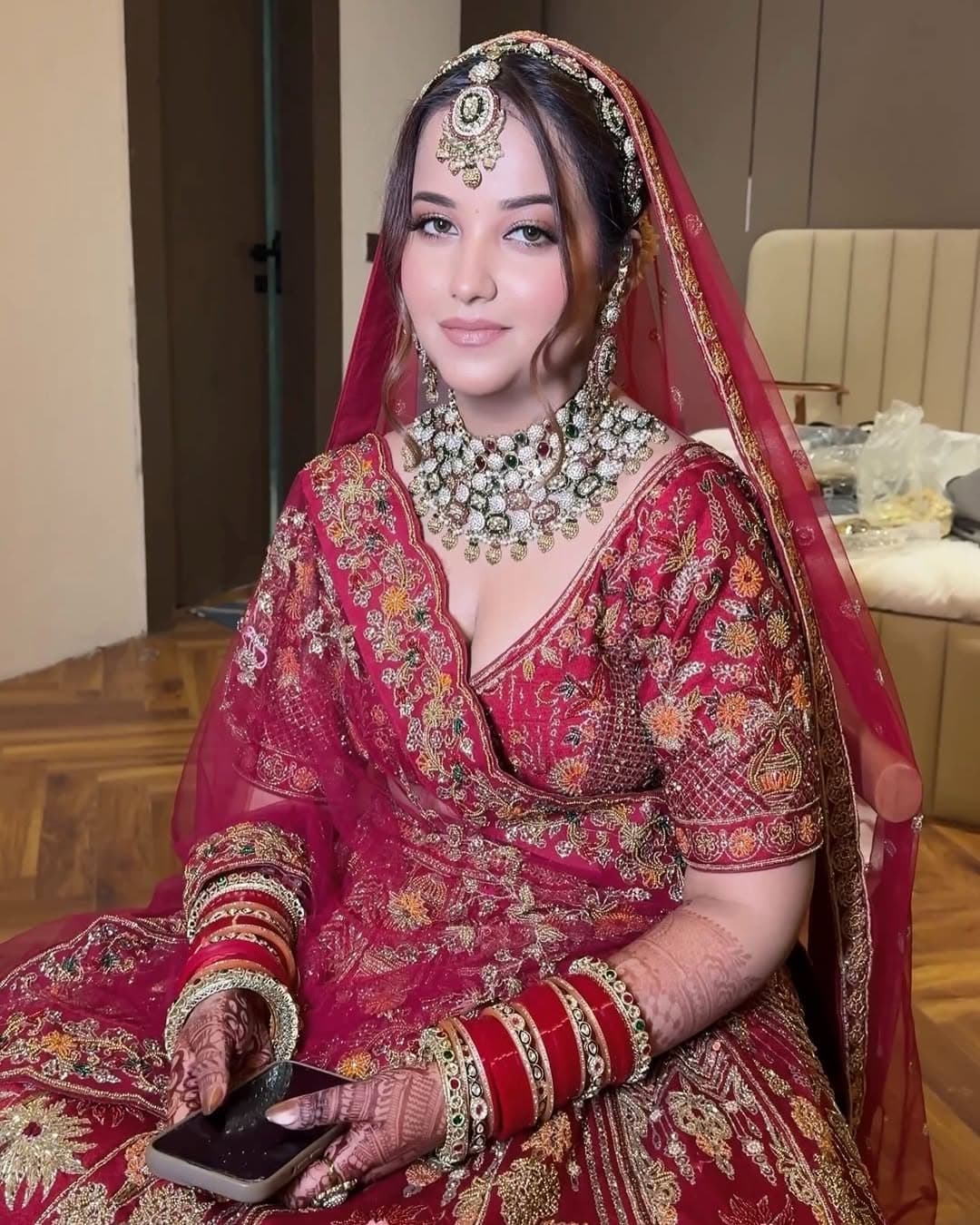 Indian bridal portrait in a richly embroidered red lehenga with layered jewelry, bridal henna, and polished wedding makeup